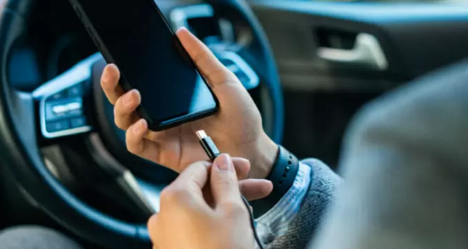 close-up e um homem usa o plugue do cabo para carregar o celular no carro,  conectando o jogo de dados do carro, música, sistema de navegação e  carregamento do celular em processo